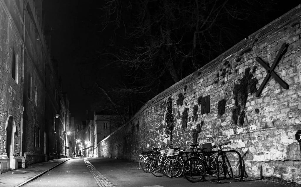 Black and white photograph of a night time empty alley between old buildings. 
