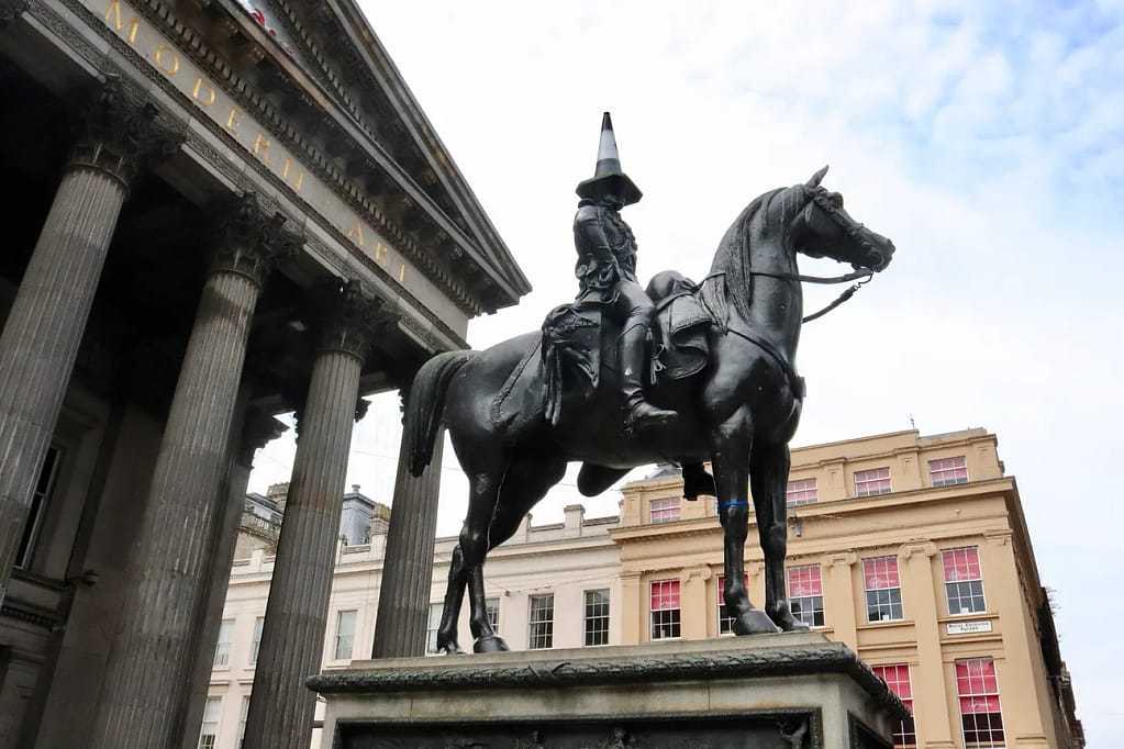 Photograph of an equestrian statue with the head of the rider covered by a black and white traffic cone