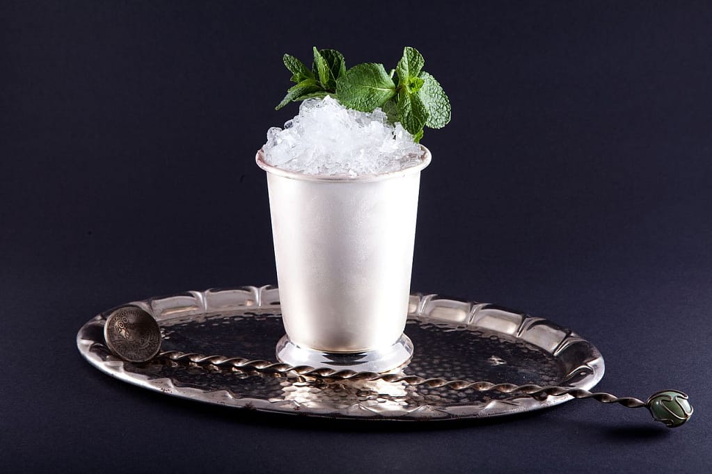 Stock image of a cocktail on a silver tray, topped with shaved ice and mint leaves.