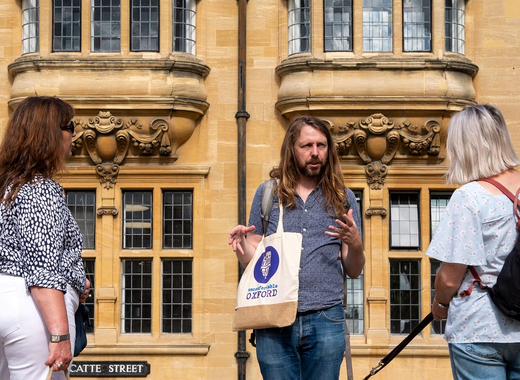 A guide talks to two attendees in front of an old building in Oxford.
