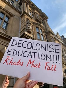 Hand holding a placard at a protest demanding the decolonisation of education.