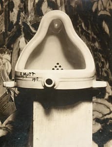 A picture of the famous 'Fountain' artwork by Marcel Duchamp, a white porcelain urinal on a wooden block.