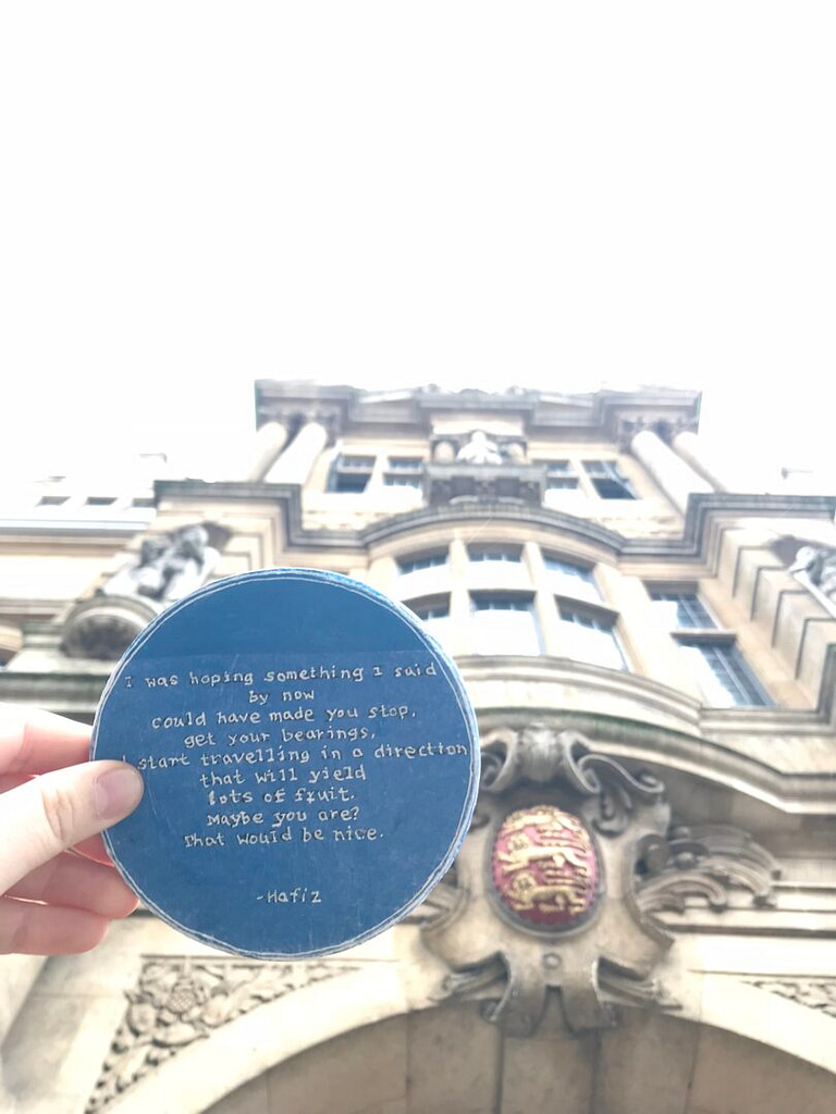 Hand holding a blue disc with writings, in front of an old building with crest - view from below