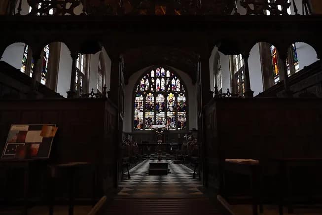Dark-lit inside of a chapel showing stained glass window.