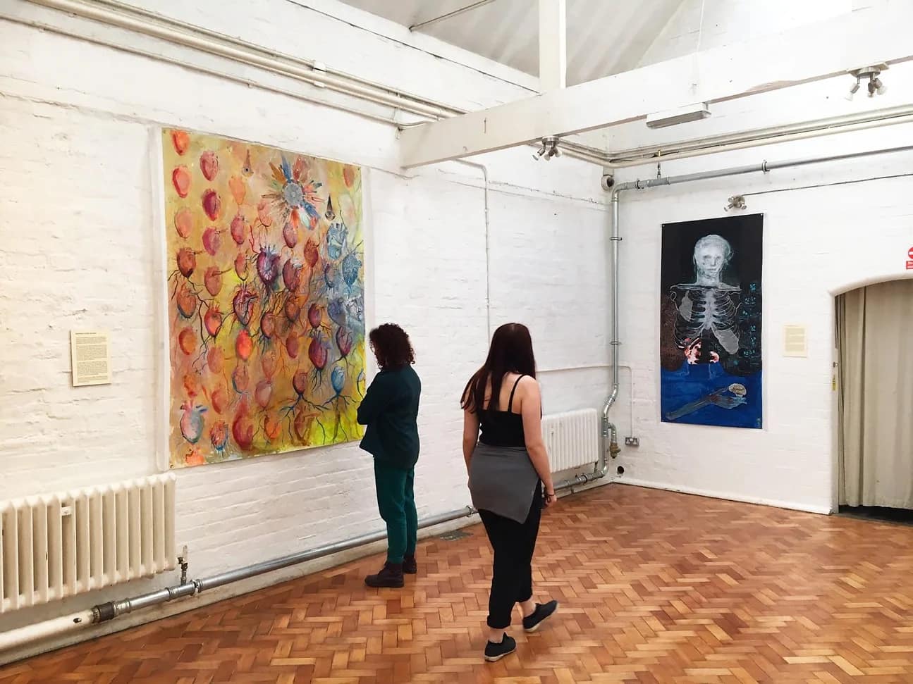Two people in an exhibition room looking at art on the walls.