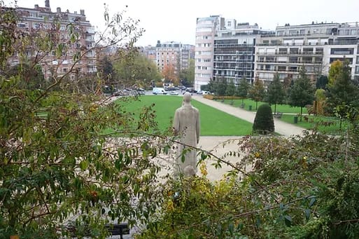 Photograph showing the back of a statue and a city park