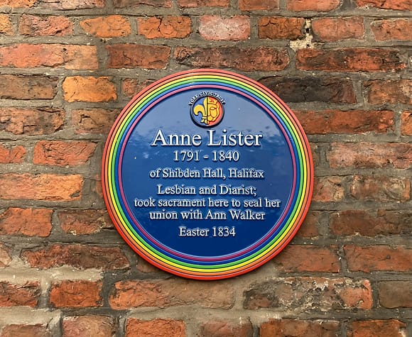 Memorial blue plaque with outer edges in rainbow colour on a brick wall