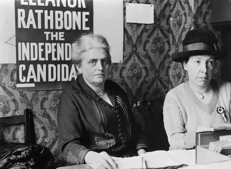 Two women taking in votes on a black and white photograph, with posters in the background.