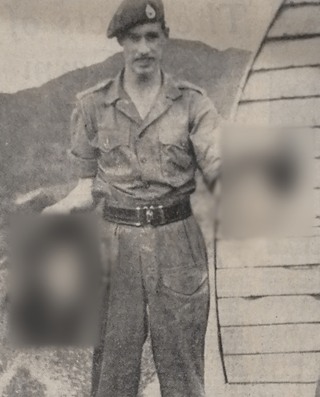 Black and white photograph of a man in a military uniform holding two (blurred and non visible) heads in his hands.