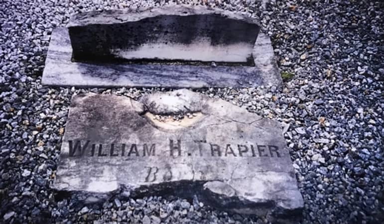 Photograph of an engraved gravestone surrounded by gravel. 